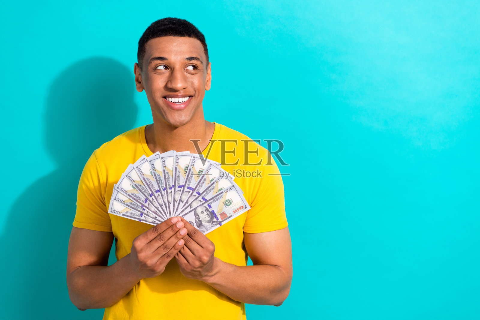 积极向上的男人的肖像，微笑着，手臂拿着美元，在绿松石色的背景上看起来空无一物照片摄影图片