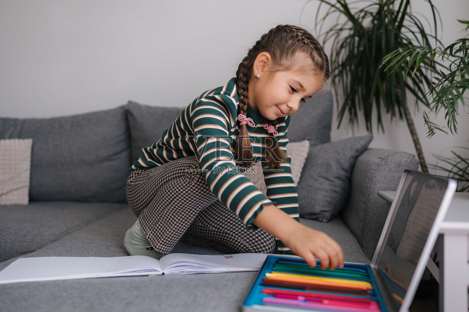 漂亮的小女孩坐在沙发上正在画册里画画。女孩用铅笔。女性微笑着看着镜头照片摄影图片