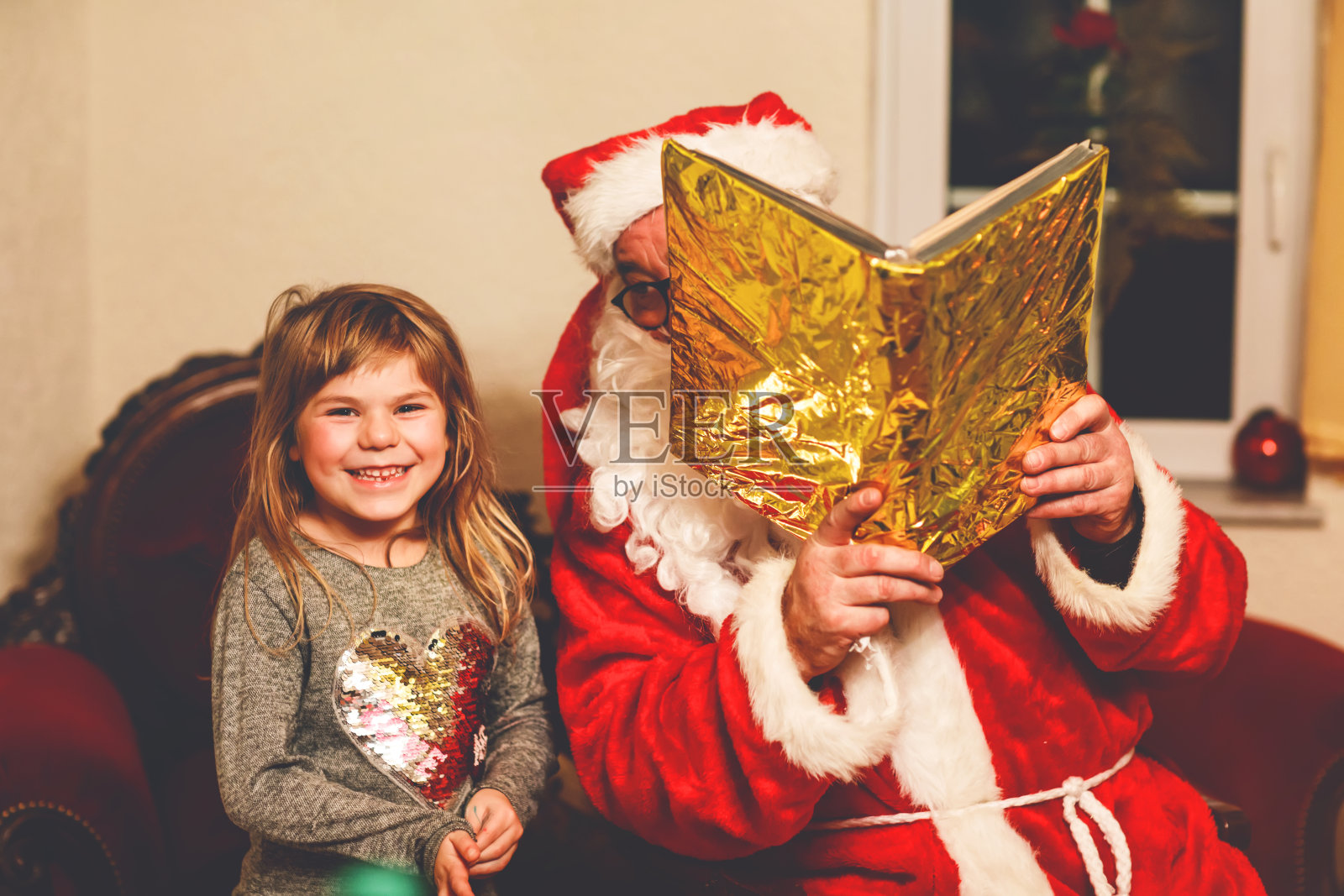 蹒跚学步的小女孩和圣诞老人交谈，用德语叫Nikolaus或Weihnachtsmann。快乐微笑的孩子等待着礼物。拿着金书的圣诞老人。圣诞节，童年，节日照片摄影图片