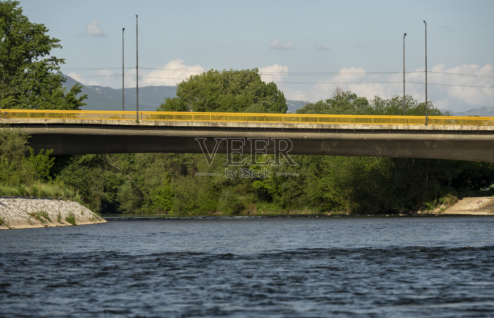 有黄色金属栅栏的河上的桥。美丽的蓝色的河流和天空与白云。照片摄影图片