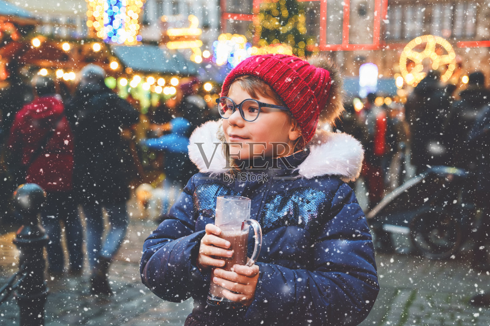 可爱的学龄前小女孩在德国圣诞市场上喝着热儿童潘趣酒或巧克力。德国传统家庭市场上快乐的孩子，穿着五颜六色冬衣的孩子照片摄影图片
