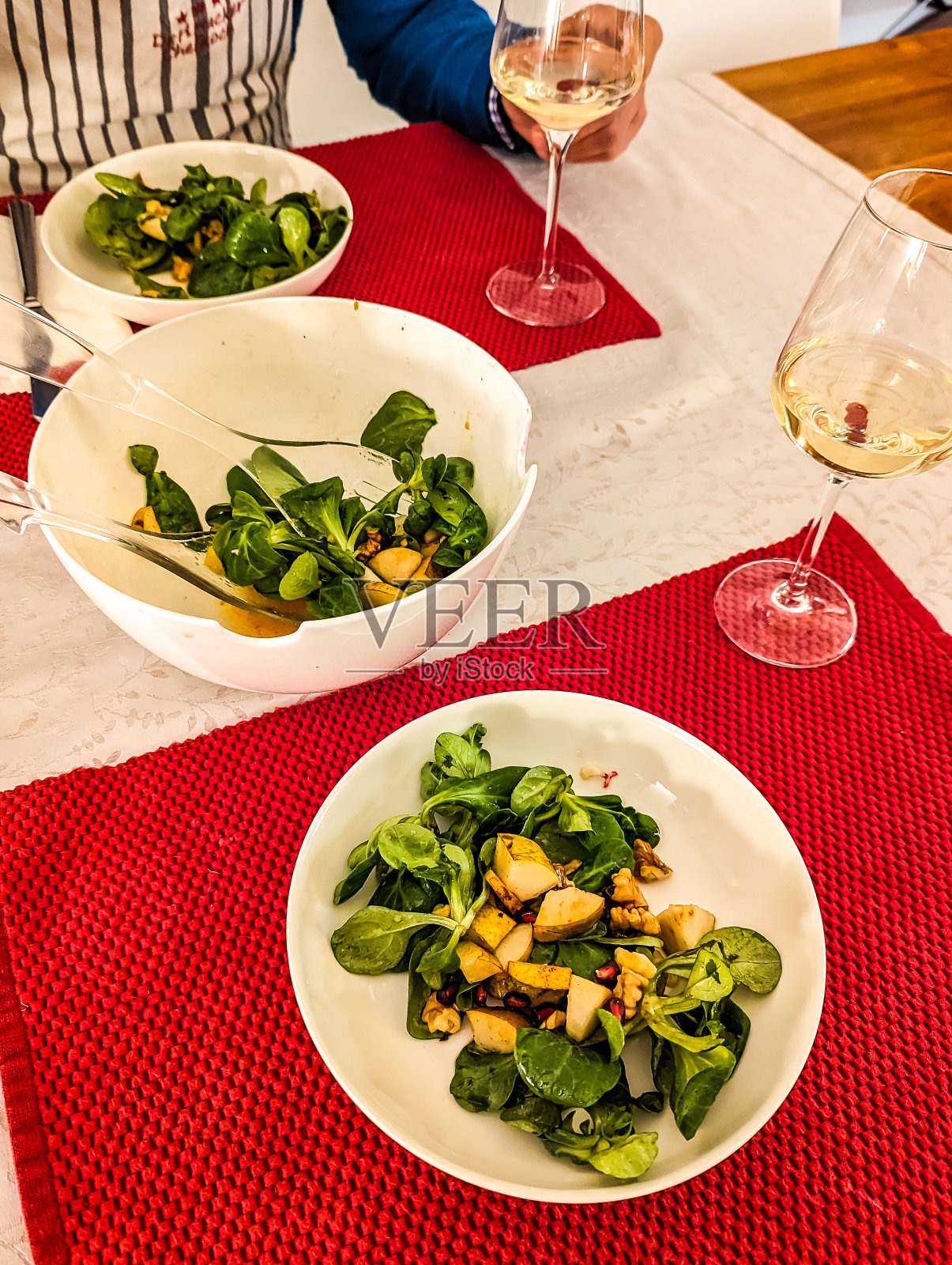 把表。沙拉碗，两个盘子，两个酒杯。羊肉生菜配梨，核桃和石榴籽照片摄影图片