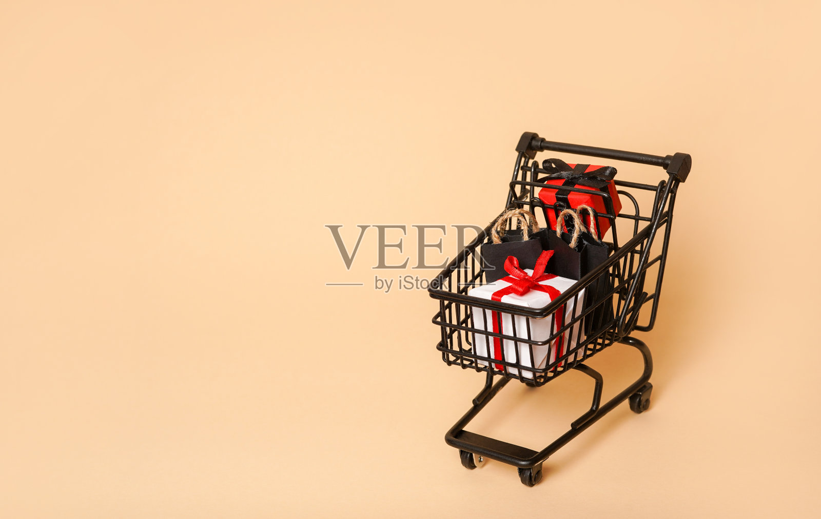 黑色购物车与纸袋和小礼盒在米色背景，复制空间。黑色星期五概念照片摄影图片