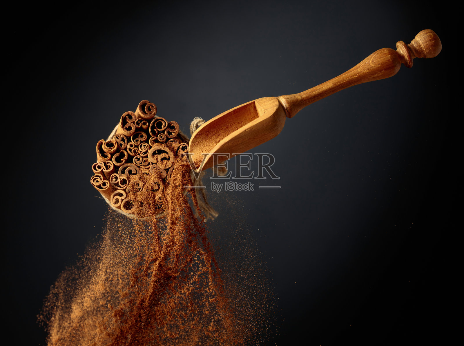 肉桂粉从木勺里倒出来。照片摄影图片