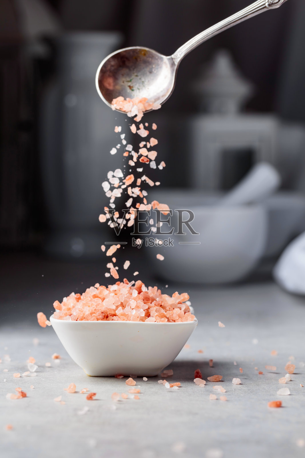 粉红色的盐结晶被倒入一个白色的小碗里。照片摄影图片