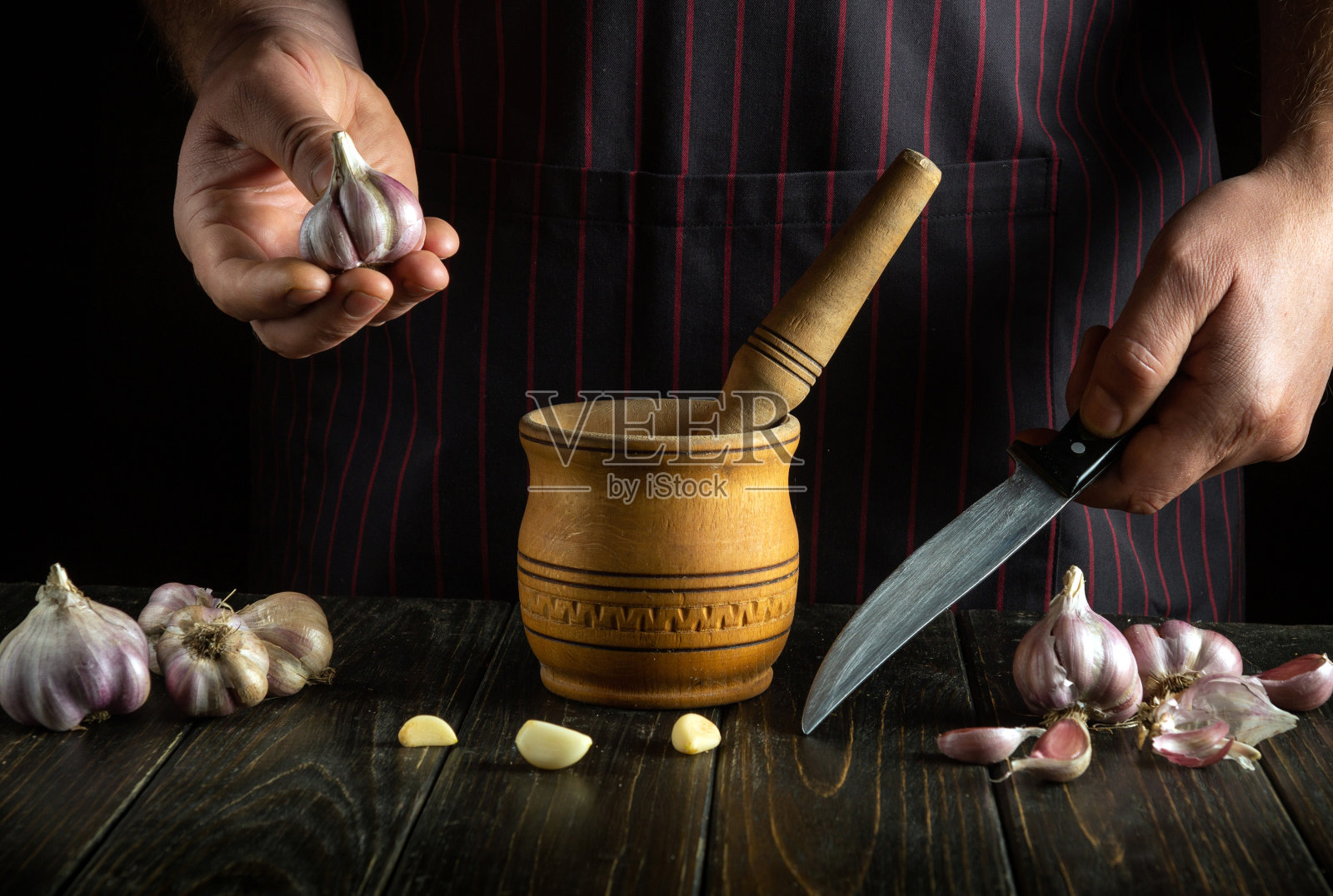 厨师手里拿着大蒜，然后用研钵把它捣碎。我们正在准备一道国菜。厨师工作时的手特写照片摄影图片