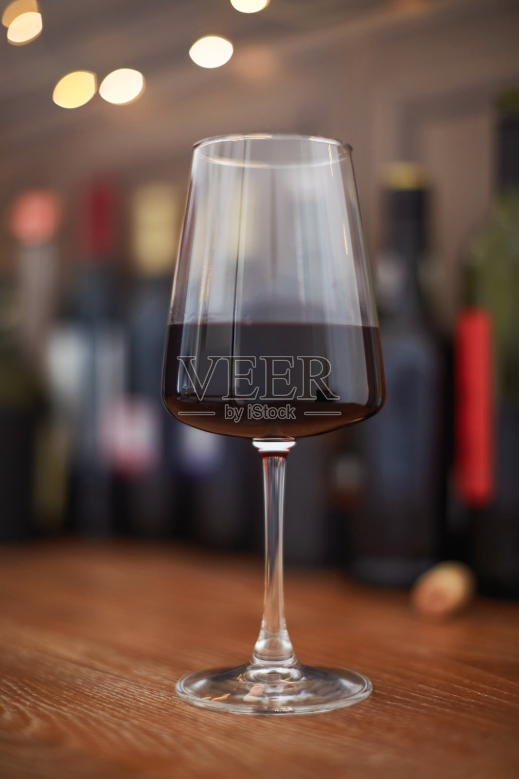 一杯红酒放在木柜台上，背景是几瓶酒照片摄影图片