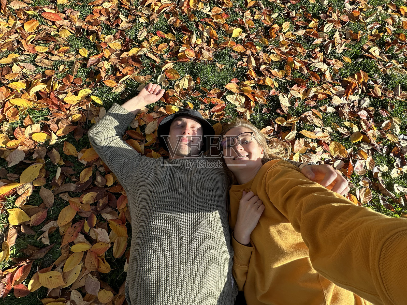 一对情侣躺在秋叶里自拍。照片摄影图片