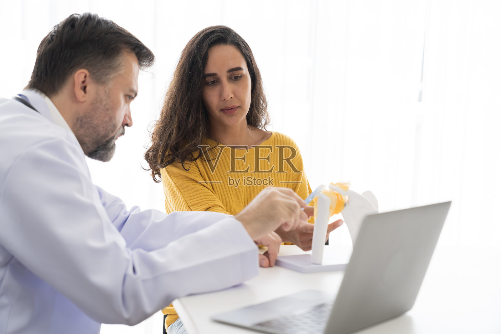 资深男医生和女病人在医院办公室一起讨论解剖学和生理学照片摄影图片