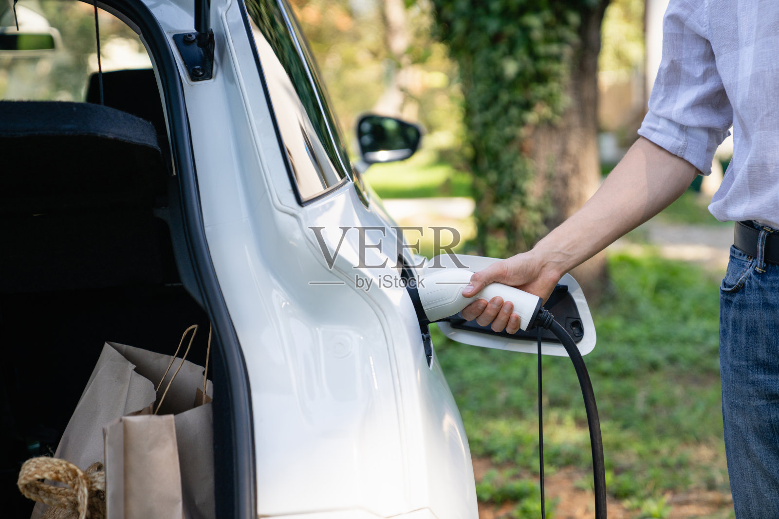 一名男子站在一辆电动车旁，手里拿着充电插头。照片摄影图片