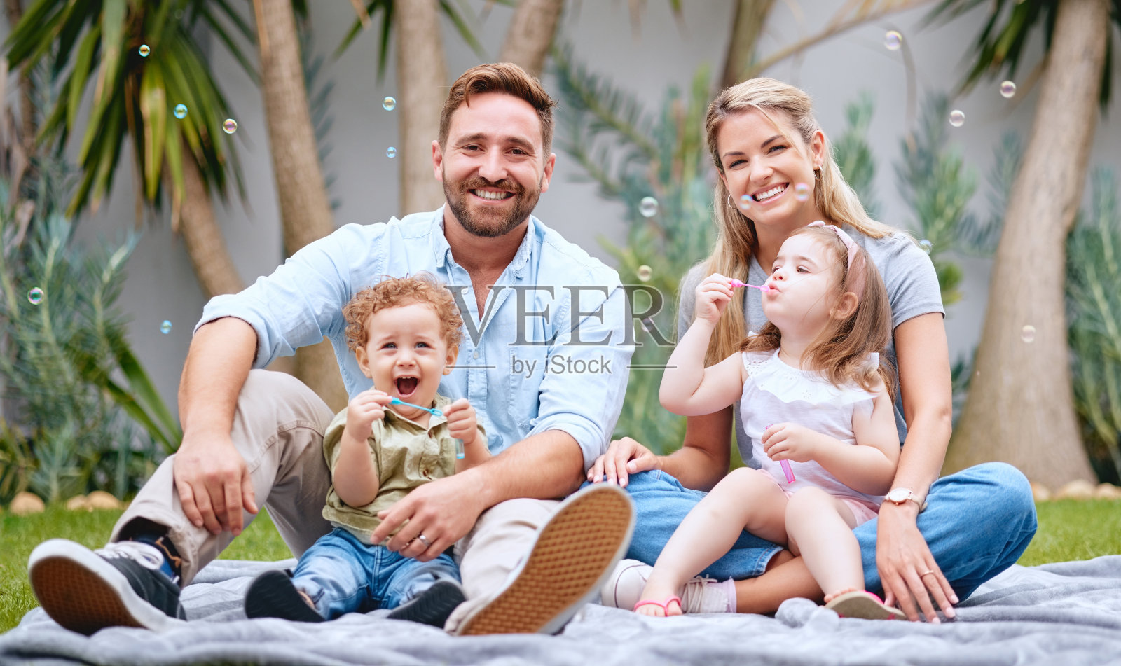 泡泡，花园和父母与孩子在周末，假期和放松的画像。家庭，爱，爸爸妈妈和孩子们坐在后院的草地上做可爱的户外活动照片摄影图片