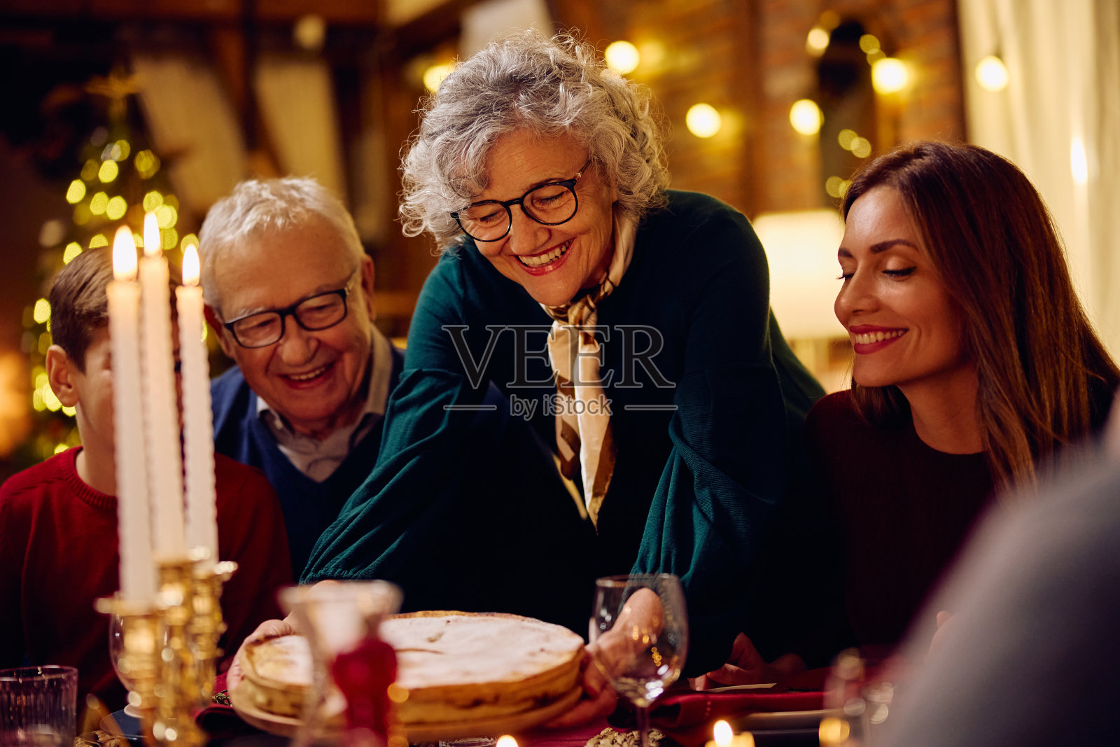 快乐的老年妇女在餐厅里为她的家人端上圣诞派。照片摄影图片