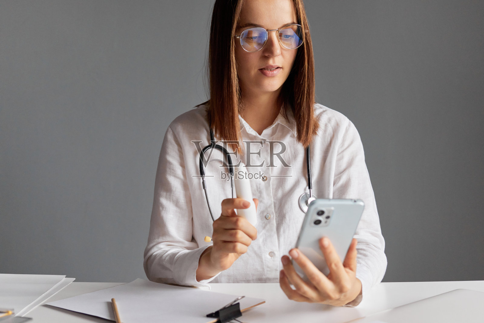 医疗从业者的工作场所。穿着白色实验室大褂的专业女医生使用智能手机进行在线咨询，为患者开出喷雾处方，并告诉患者如何服用。照片摄影图片