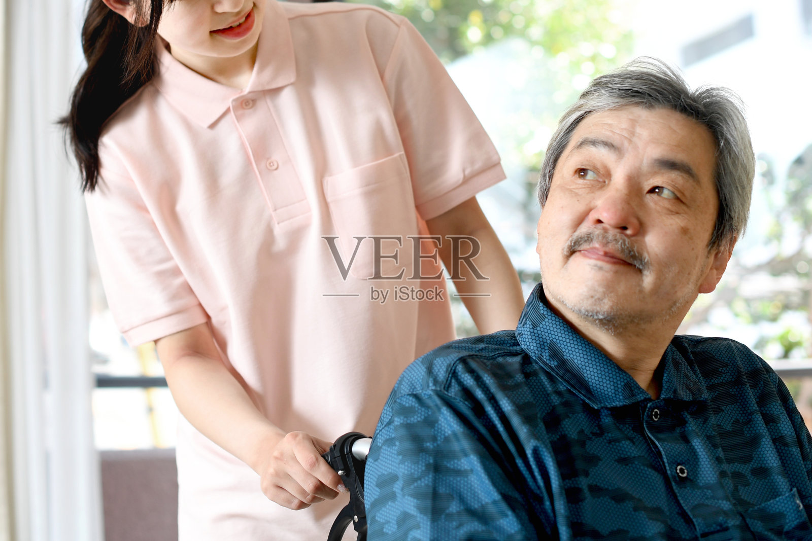 一位年轻的女护工正在帮助一位坐在轮椅上的白发亚洲老人照片摄影图片