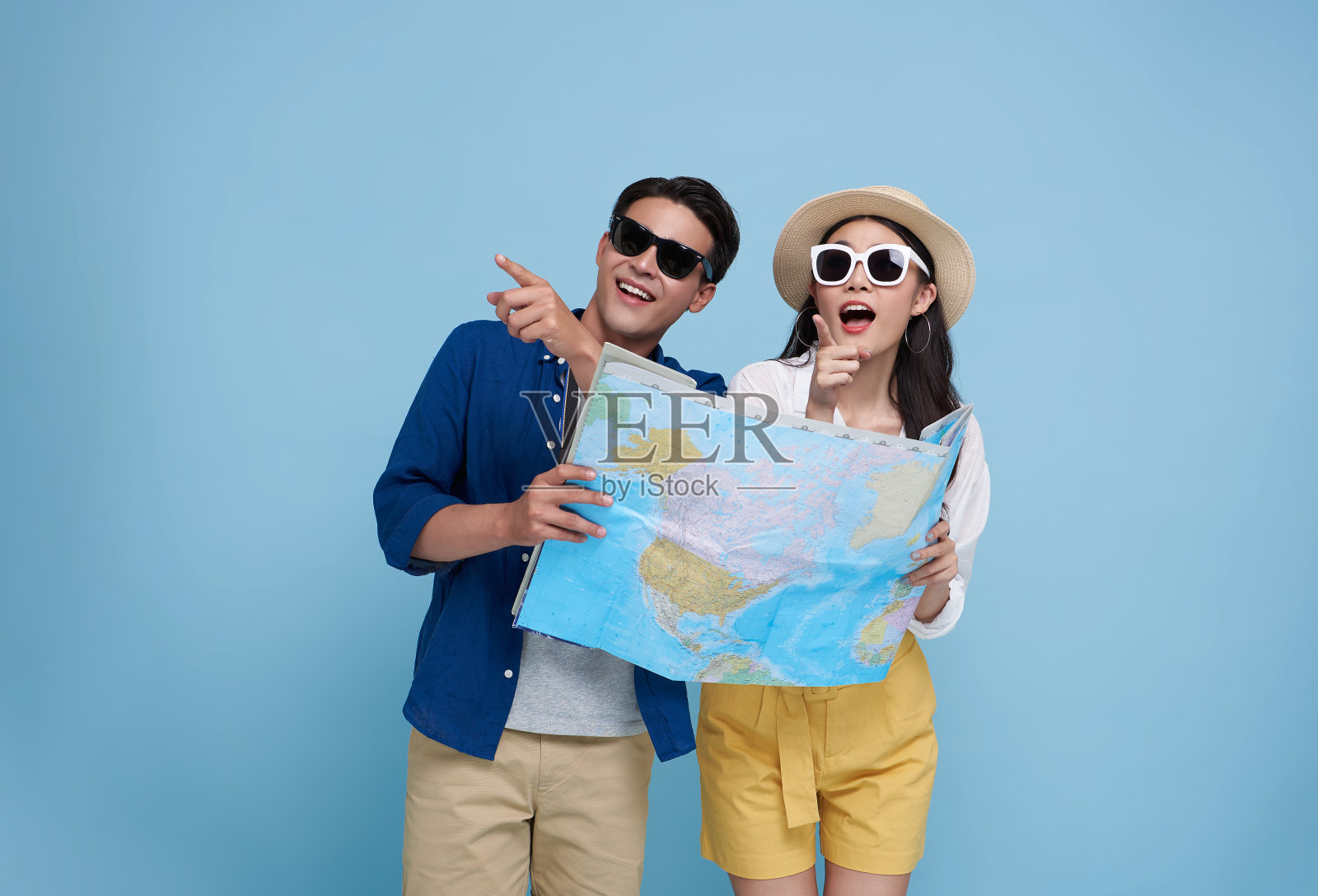 幸福的亚洲夫妇游客看地图，手指着复制空间，带着行李去旅行，孤立的蓝色背景。照片摄影图片
