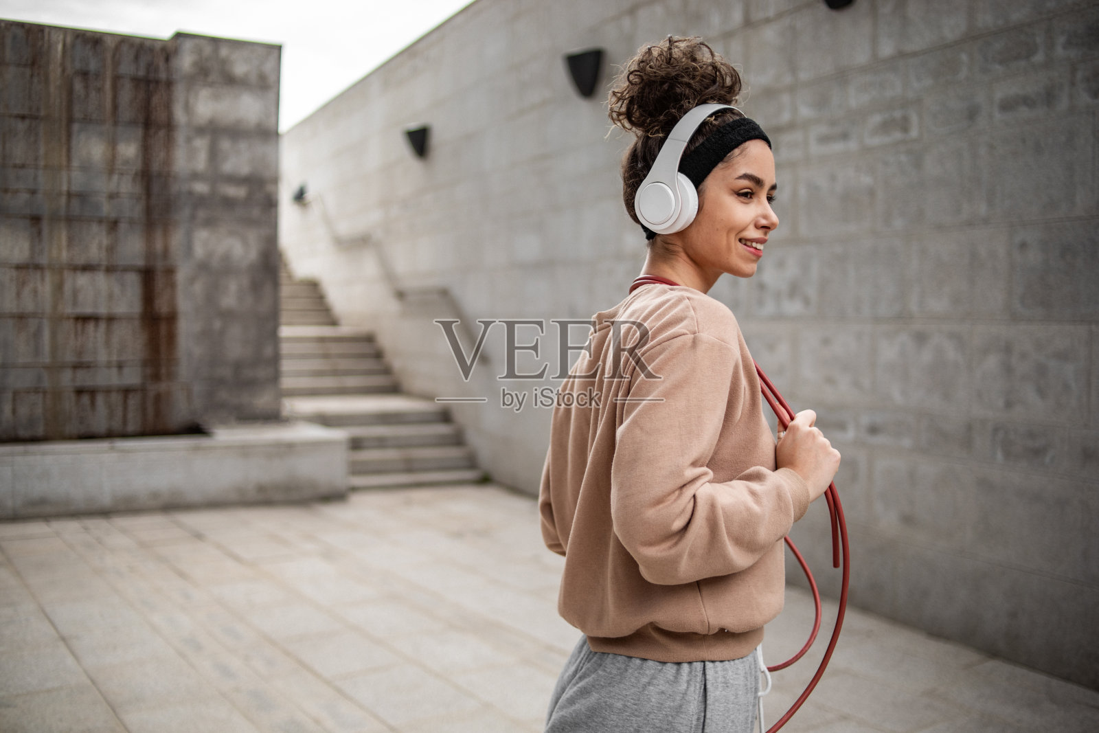 这是一位年轻的女运动员在水泥墙旁摆姿势的照片，她结束了跳绳的运动训练照片摄影图片