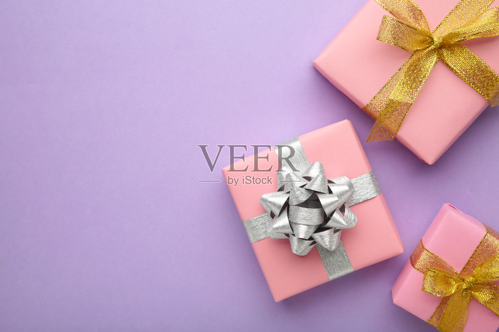 粉红色的礼品盒与银和金弓在紫色的背景。照片摄影图片