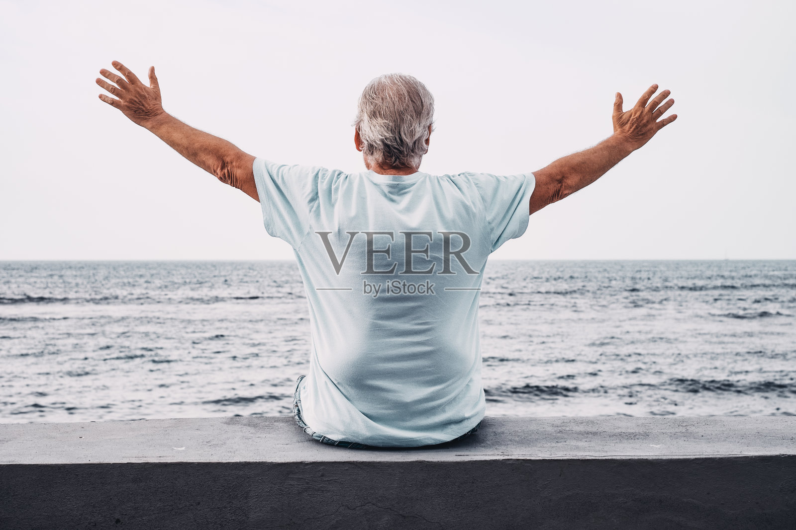 老人的后视图，张开双臂，面对大海，在日出时看着地平线，享受自由和退休照片摄影图片