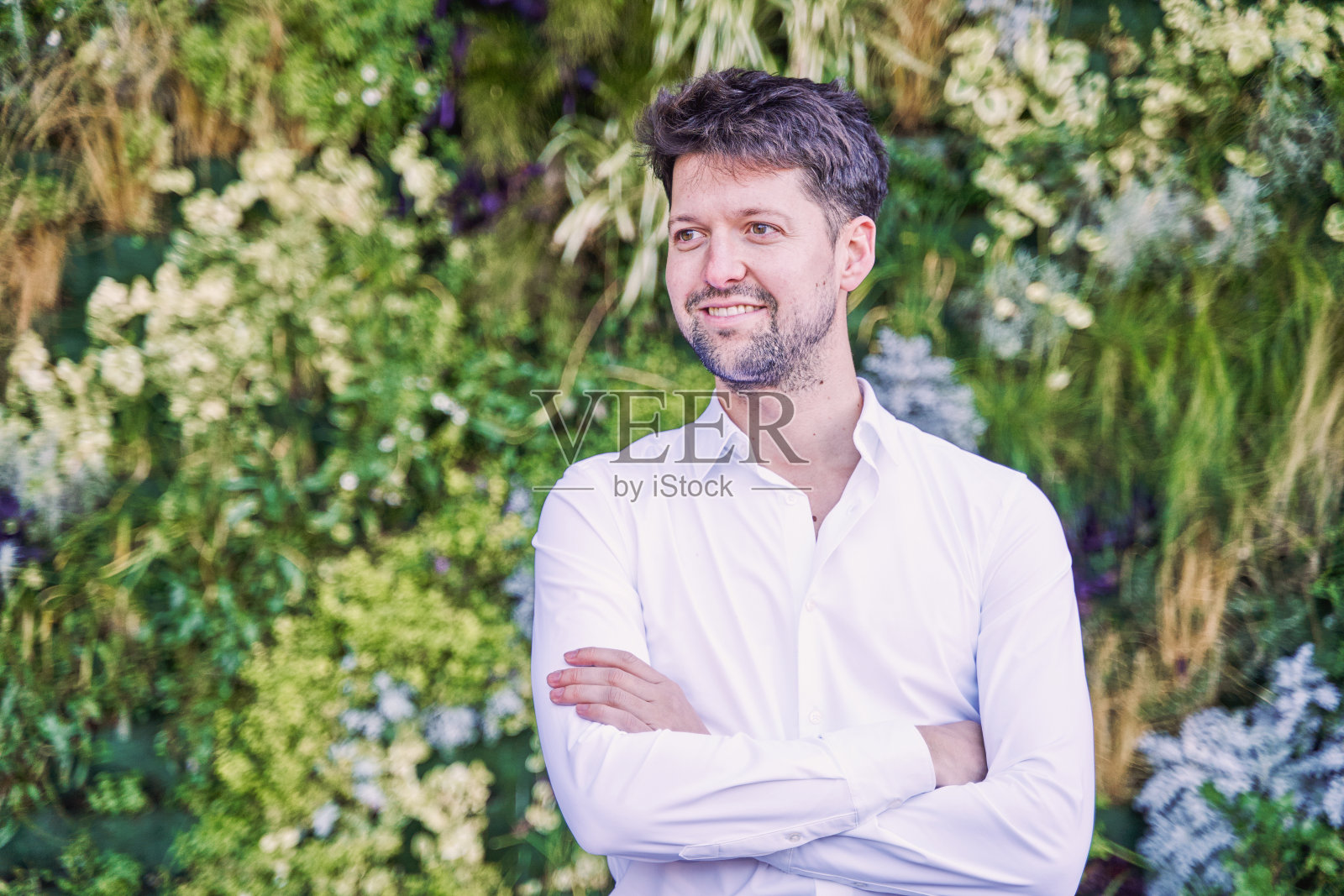 一个留着胡子、牙齿完美的年轻白人男子在垂直花园上摆姿势照片摄影图片