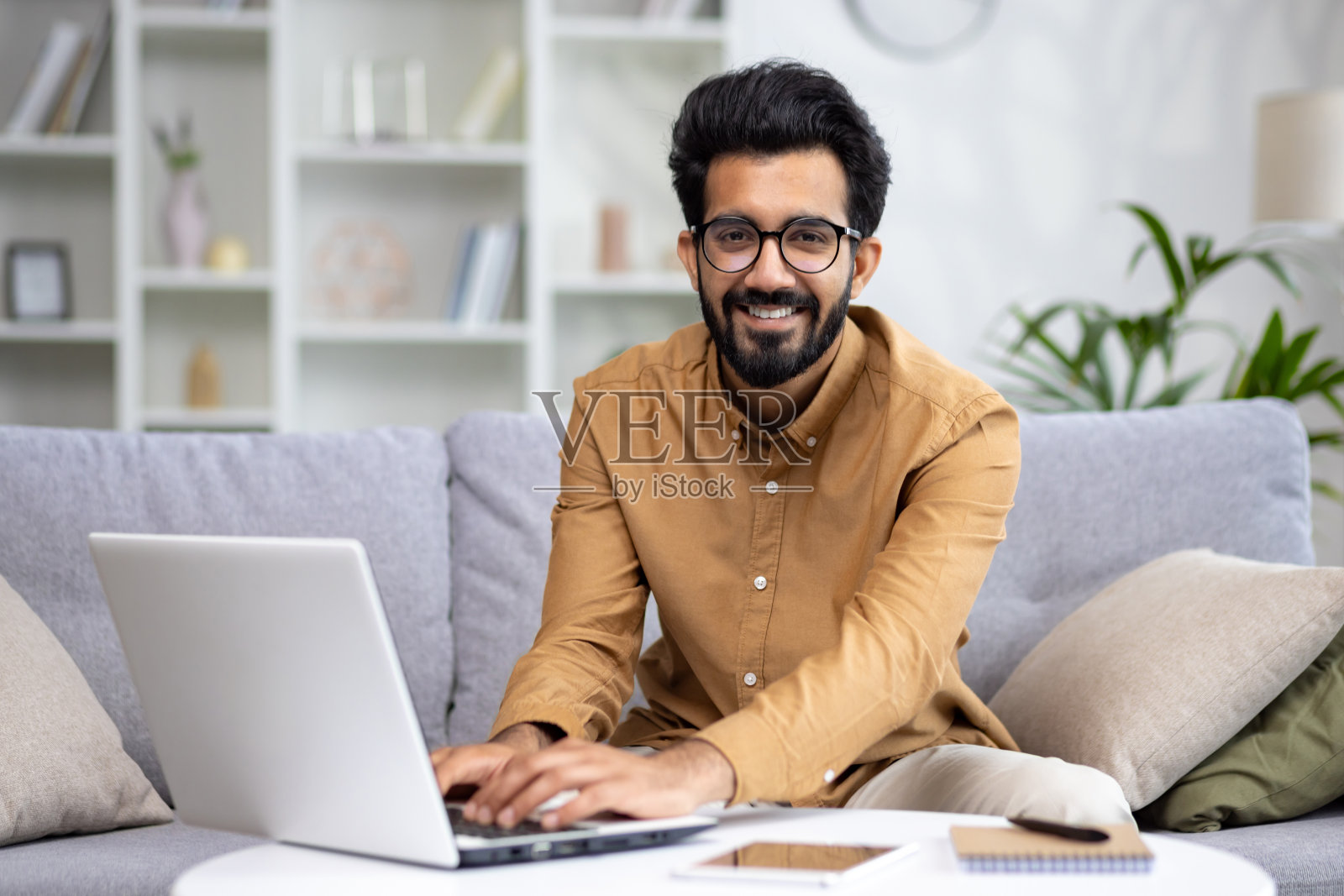 年轻穆斯林商人的肖像，自由职业者在家用笔记本电脑工作。在键盘上打字，对着镜头微笑照片摄影图片