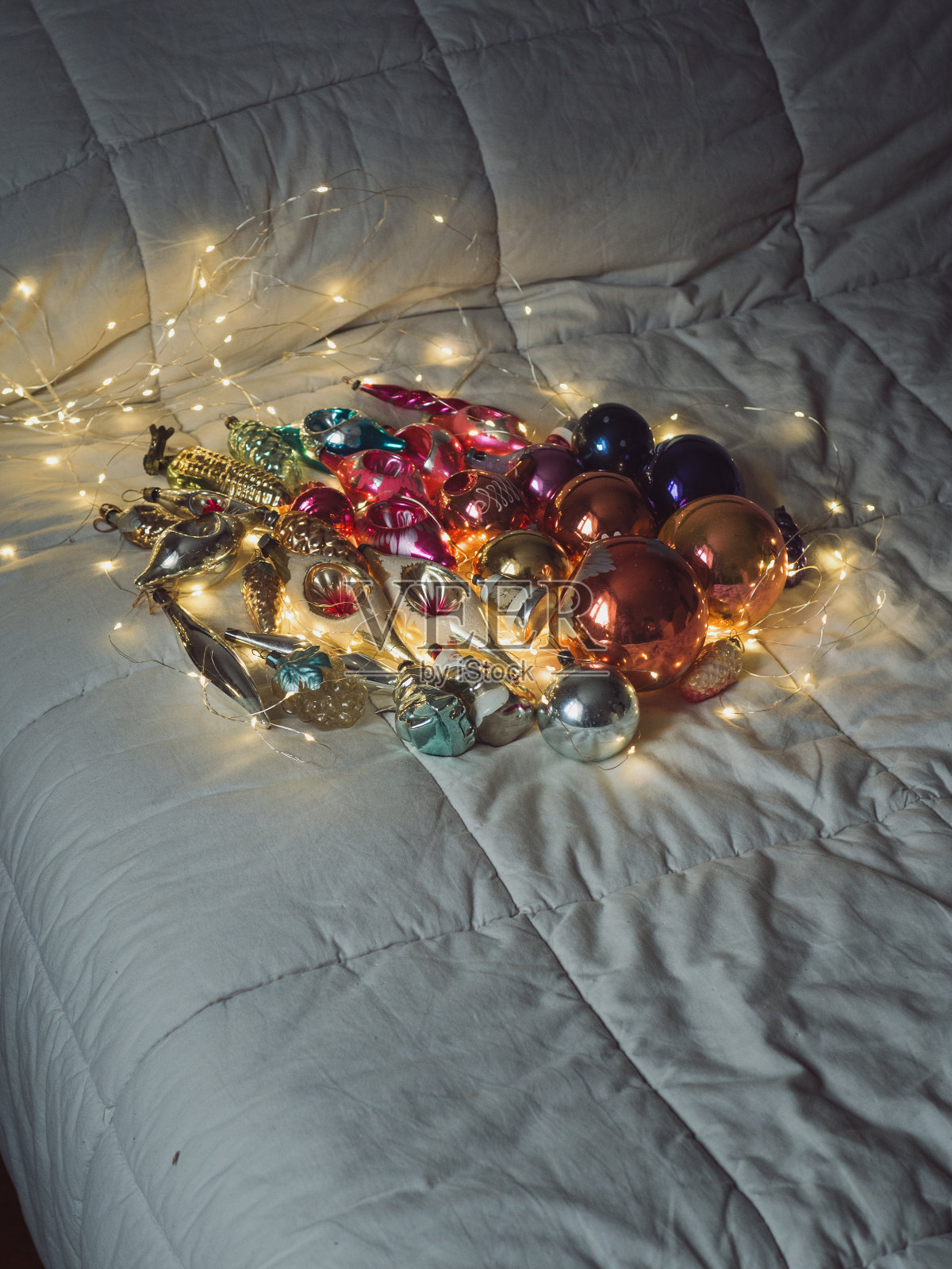 老式吹制玻璃圣诞装饰品的垂直特写，摆放在床上，用电灯照亮。照片摄影图片