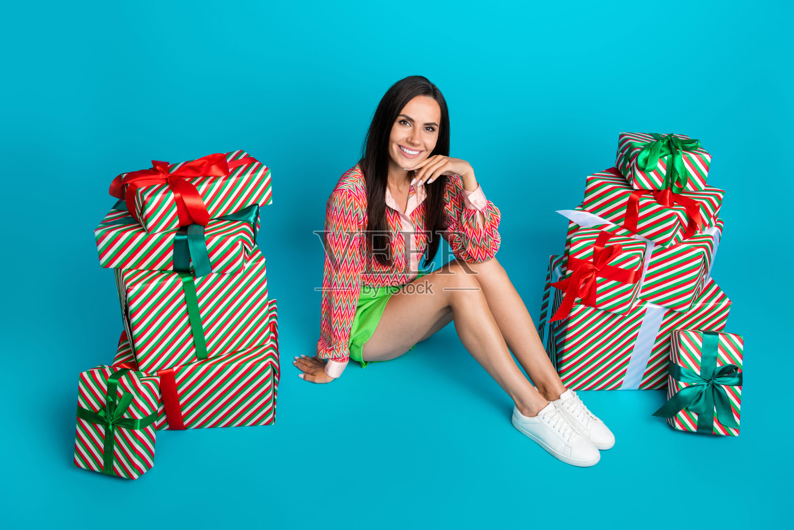 迷人的年轻女子的全身照片坐在地板迷人的礼物堆穿时髦的绿色裙子孤立的青色背景照片摄影图片