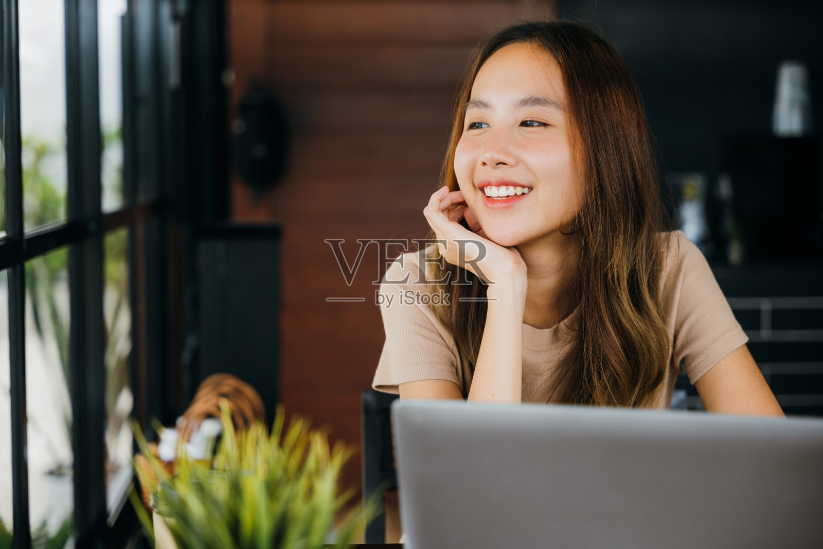 女商人微笑着独自坐在咖啡桌旁，拿着笔记本电脑，看着窗外照片摄影图片