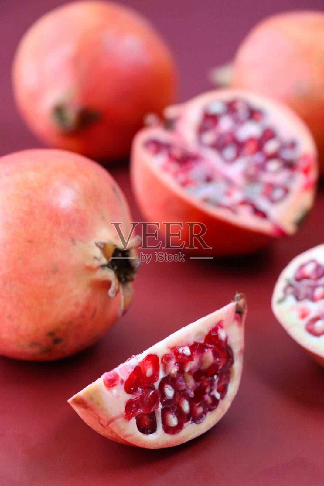 石榴(Punica granatum)的特写图像，整个，一半和四分之一的水果切片，显示红粉红色的果皮(外果皮)，白色的中果皮(反照率)和红色的果肉(果皮)包围着种子，红色背景，重点在前景照片摄影图片