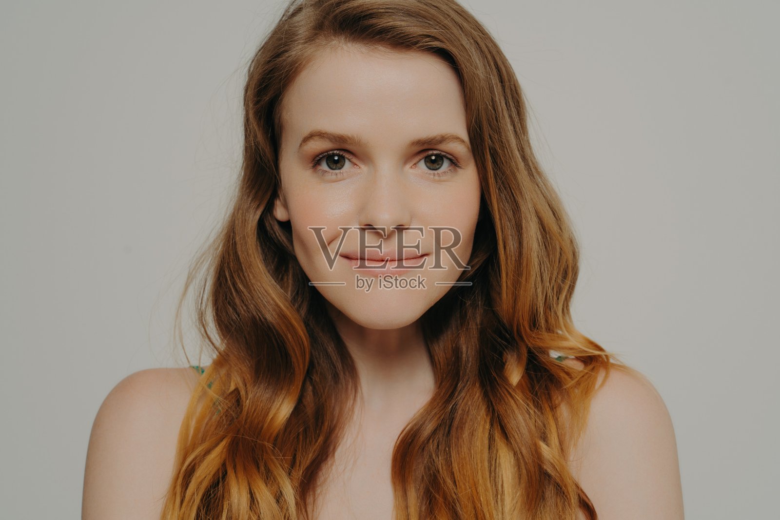 宁静的美女，有着微妙的微笑和波浪的头发，在中性的背景下穿着芥末色的上衣照片摄影图片