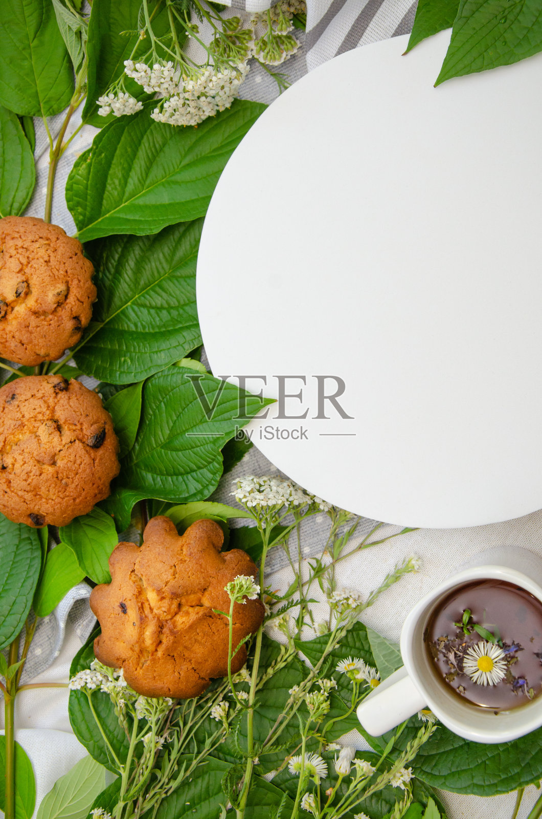 松饼和一杯草药茶，白色圆形讲台，木制盘子和棉花桌布上的季节草药。食谱或食物菜单模板照片摄影图片