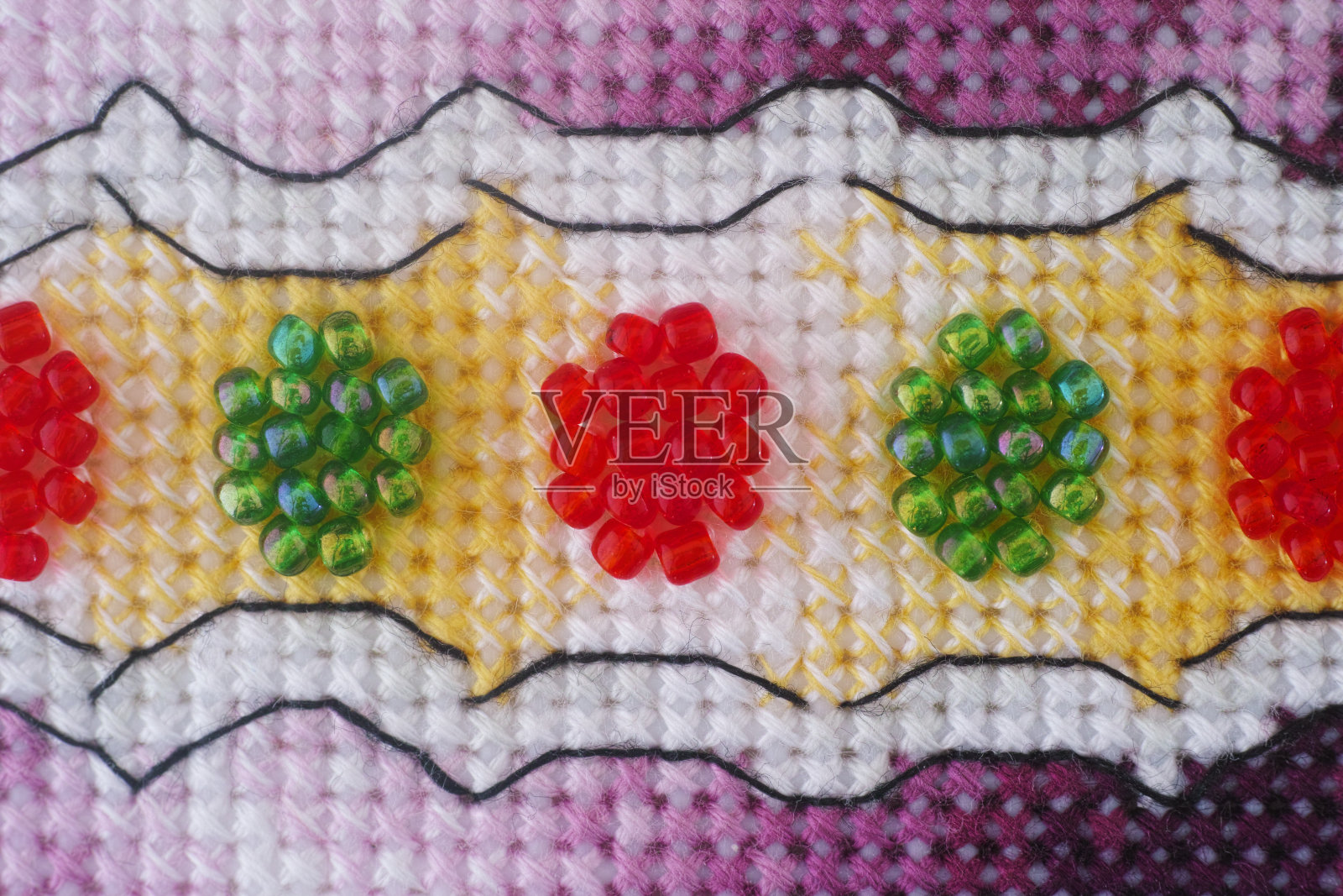 用紫色、黄色和白色的线以及红色和绿色的珠子制成的十字绣的特写镜头。照片摄影图片