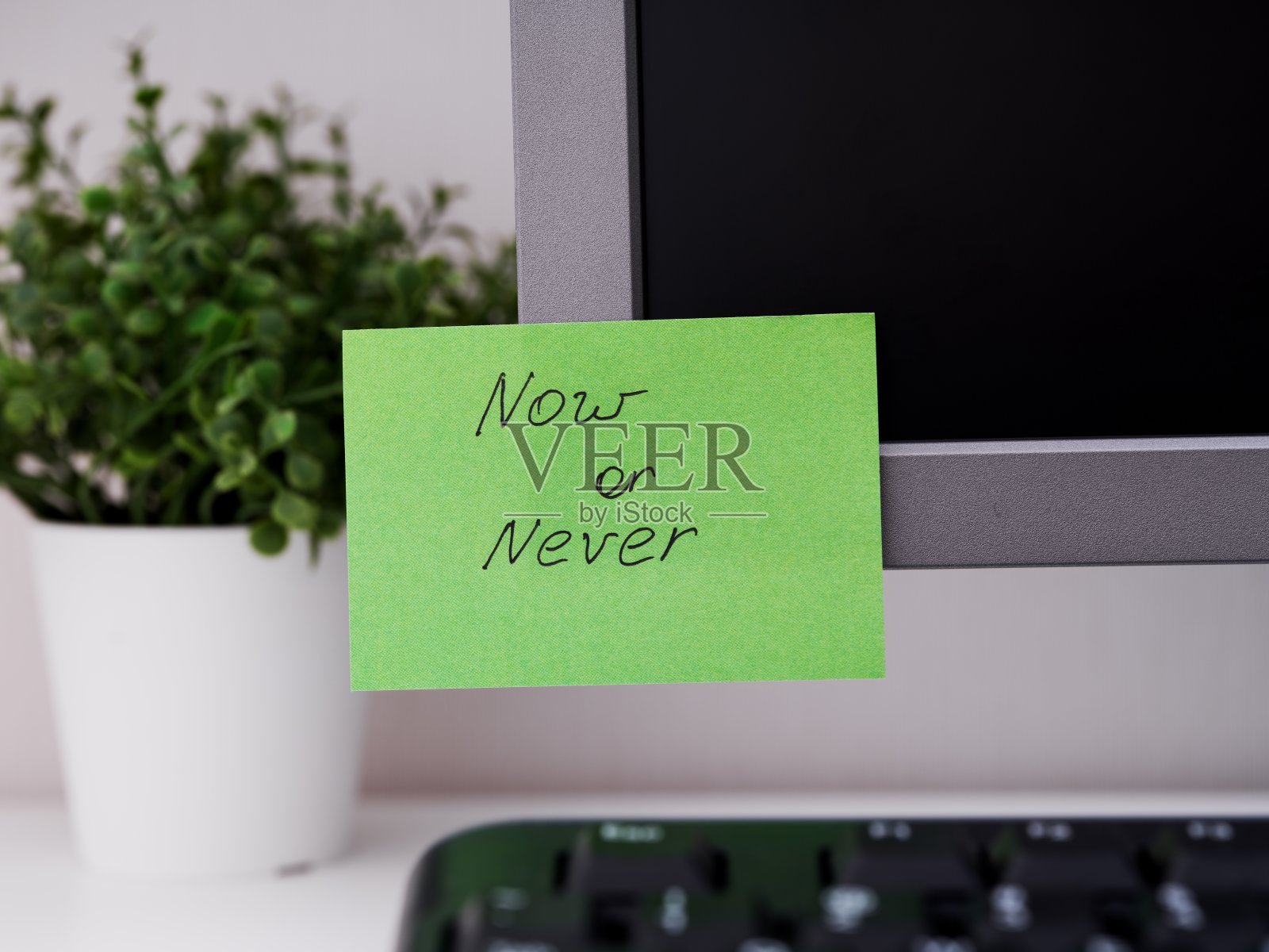 在办公室的显示器上贴一张绿色的纸，上面写着“现在或永远”的提醒。照片摄影图片