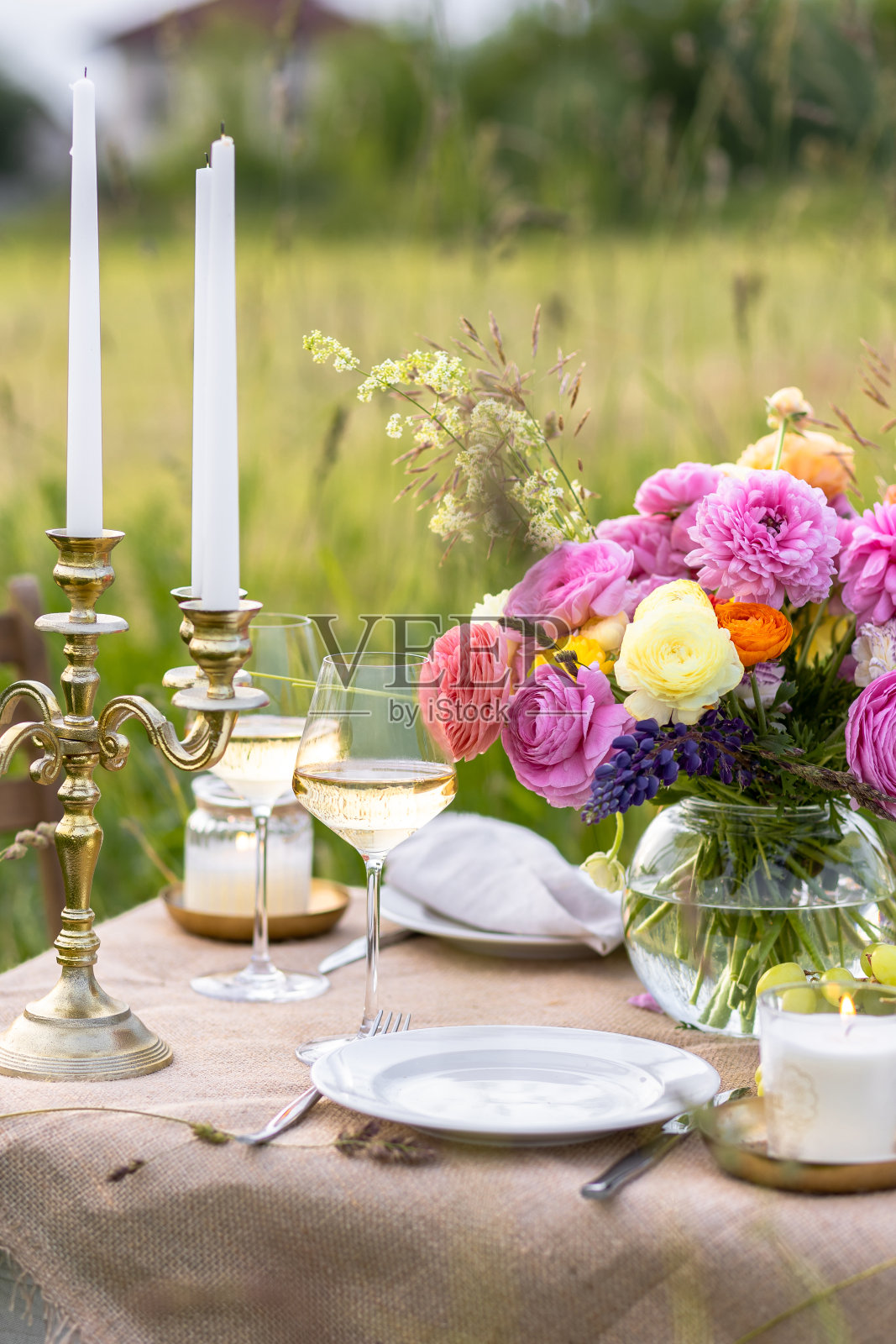 美丽的乡村婚礼浪漫的晚餐装饰在一个盛开的草地与紫色紫罗兰羽扇豆花。花瓶，葡萄酒杯，樱桃和杏。木桌，篮子。日落，黄金时刻，夏天照片摄影图片