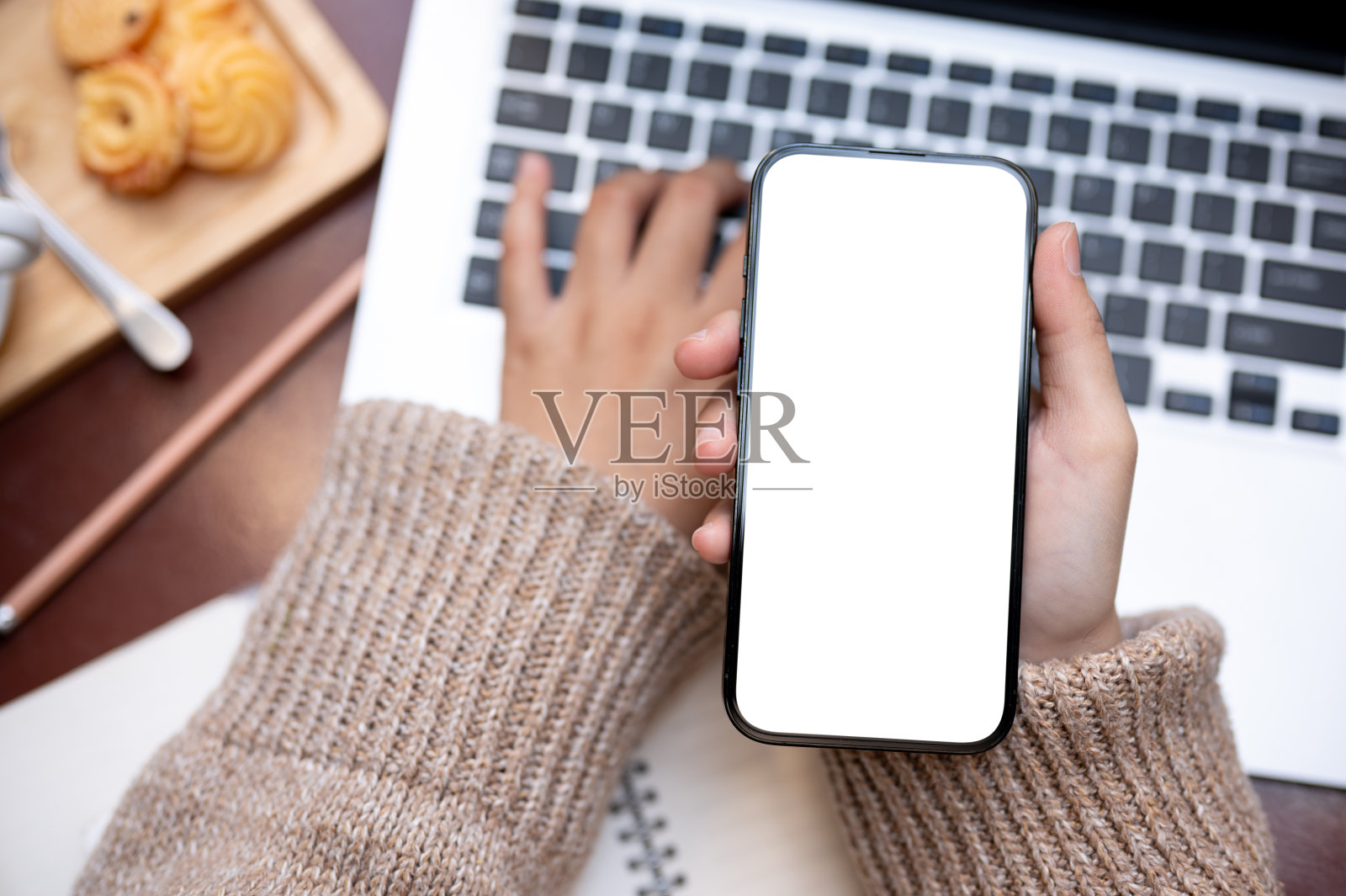 一位女士坐在咖啡馆的桌子上，一边用笔记本电脑一边用智能手机工作。照片摄影图片