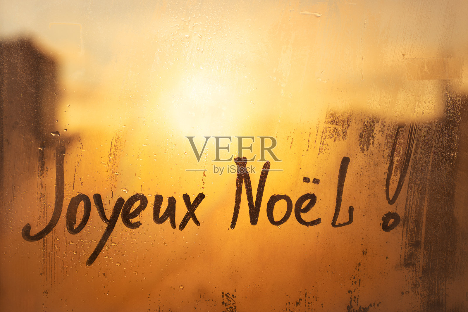 夕阳下，城市泥泞潮湿的橙色窗户上，用英语写着法语Joyeux Noel圣诞快乐照片摄影图片