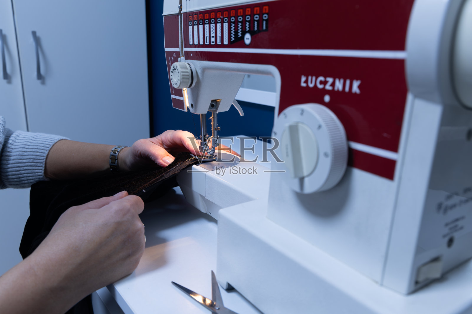 在修理衣服的机器上缝纫。女裁缝在缝纫室的机器上缝纫照片摄影图片