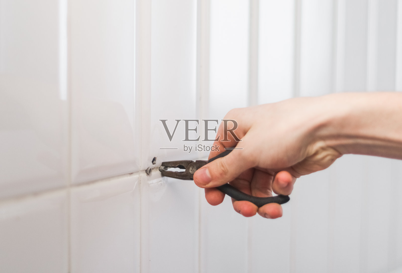 一个年轻人用钳子从墙上拔出一个销子。照片摄影图片