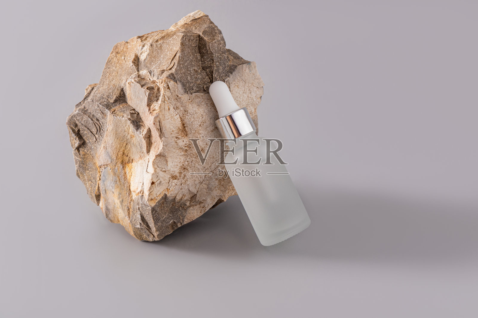 一个有机护肤品的哑光滴管瓶靠在一块有质感的大石头上。天然的化妆品。灰色背景。照片摄影图片