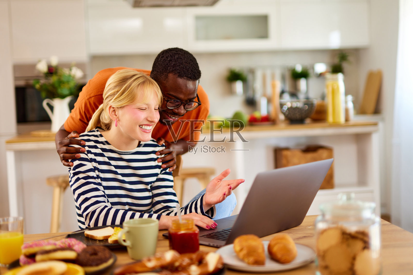 年轻的多种族夫妇在家里边吃早餐边用笔记本电脑聊天照片摄影图片