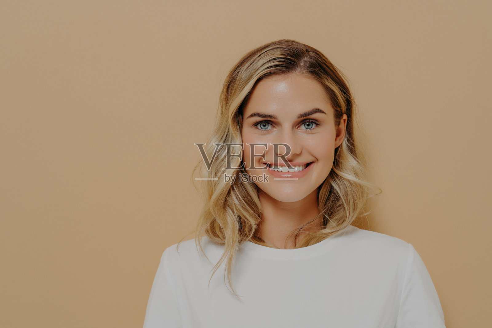 容光焕发的年轻女子带着温暖的微笑，穿着一件休闲的白色上衣，背景是柔和的米色照片摄影图片