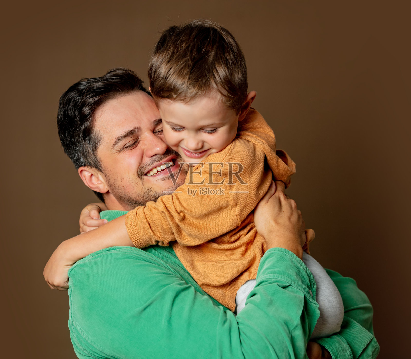 父亲和儿子愉快地拥抱在棕色背景照片摄影图片