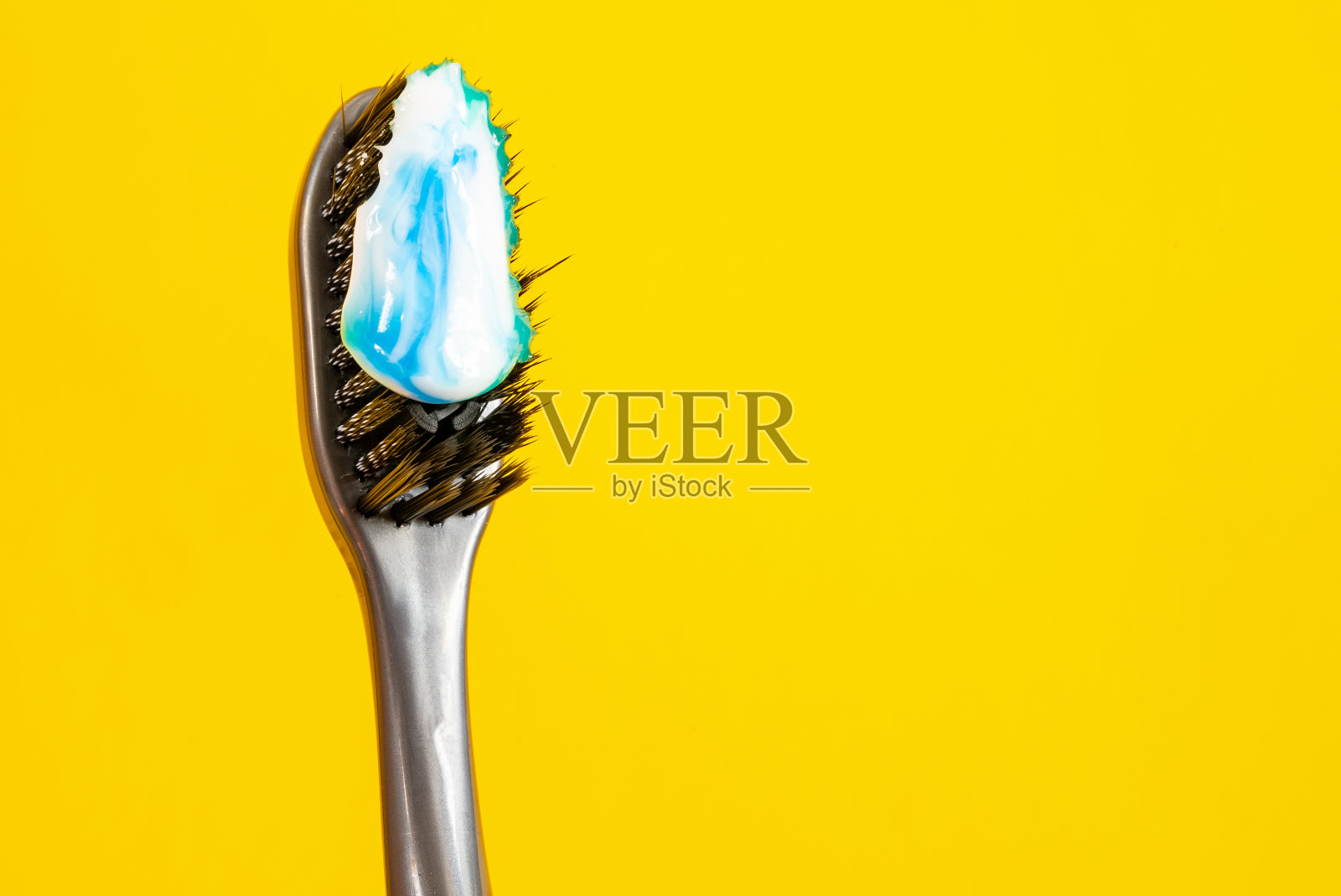黑色刷毛牙刷，黄色背景上有白色和蓝色的牙膏照片摄影图片