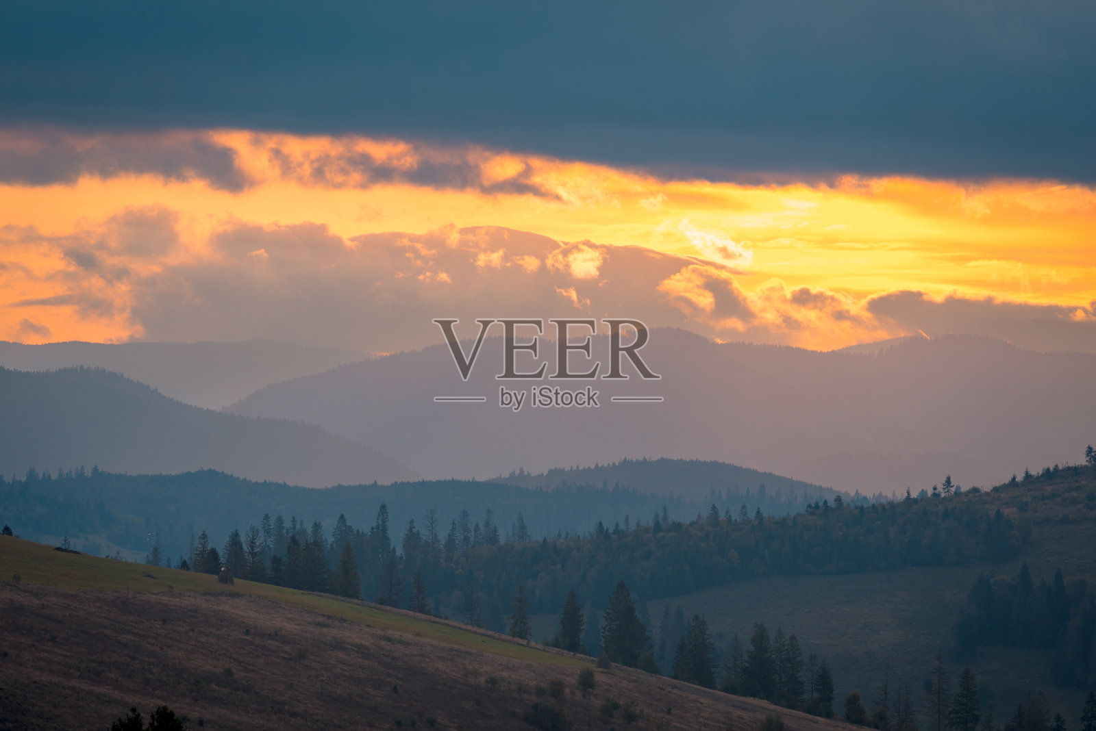 喀尔巴阡山脉的小山丘在日出的五彩多云的天空下。照片摄影图片