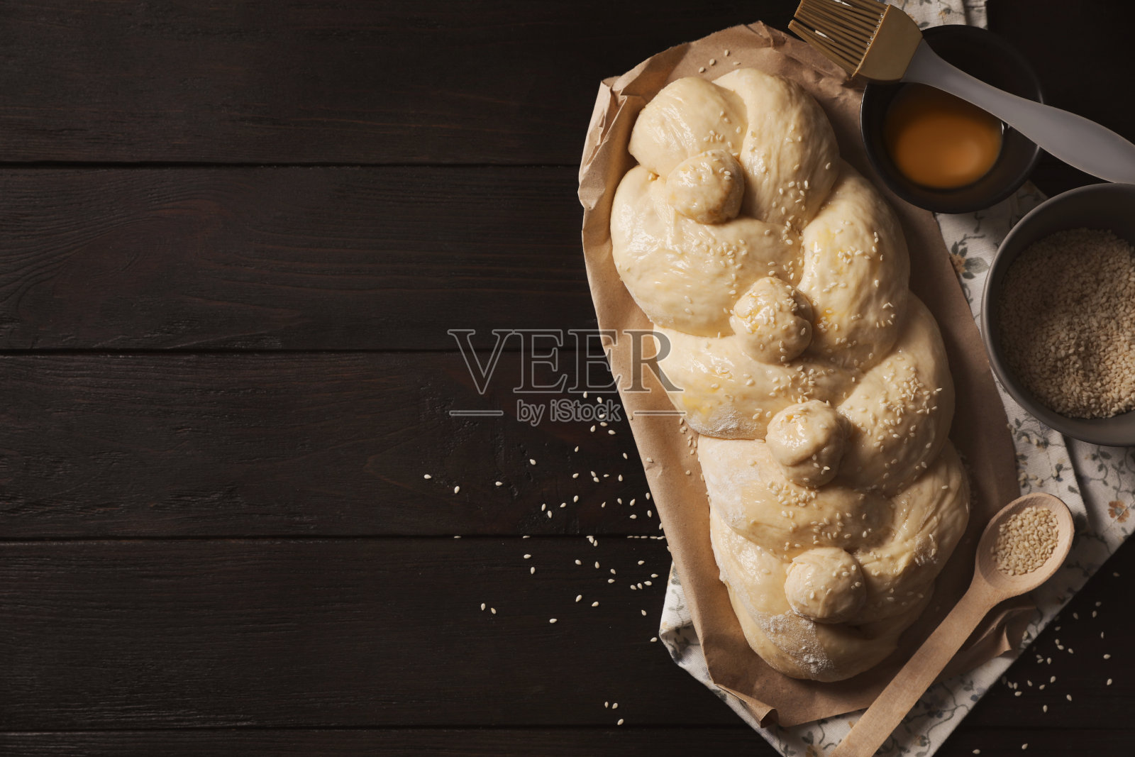 生的编织面包，配料和糕点刷在黑色的木桌上，平铺着文字的空间。传统的安息日挑战照片摄影图片