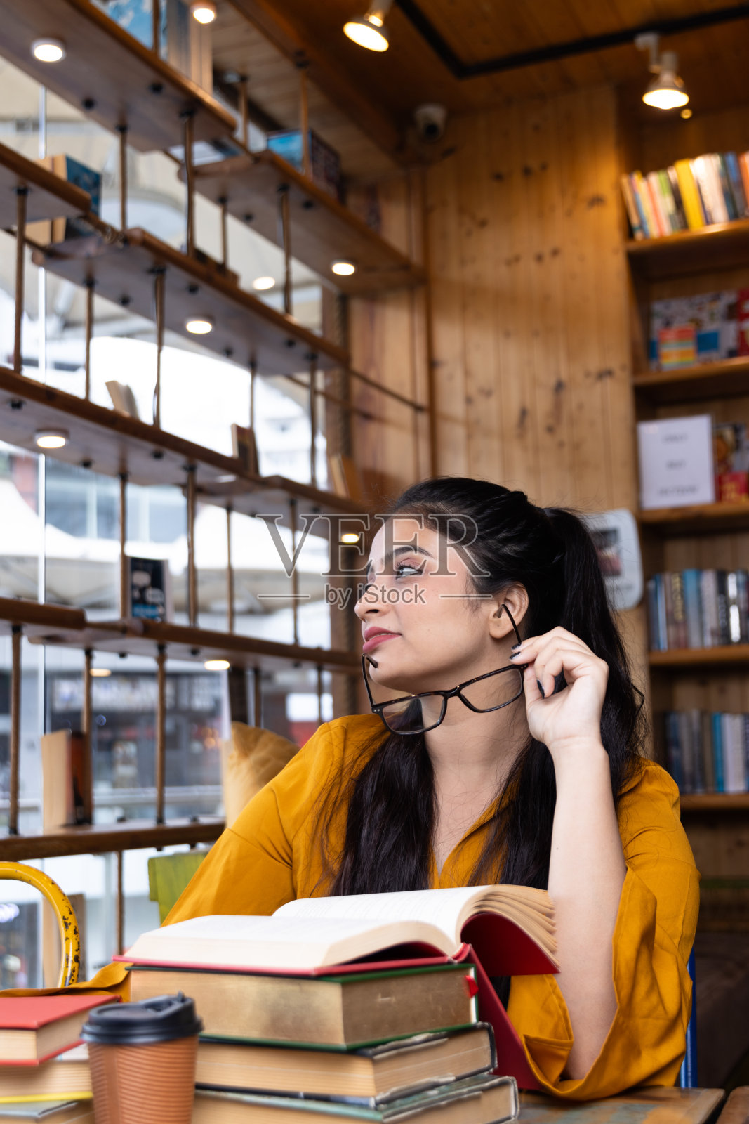 一个漂亮的年轻女孩，商业女性或学生坐在一堆书，在学校或大学图书馆工作或学习，或在公司办公室坐在书照片摄影图片