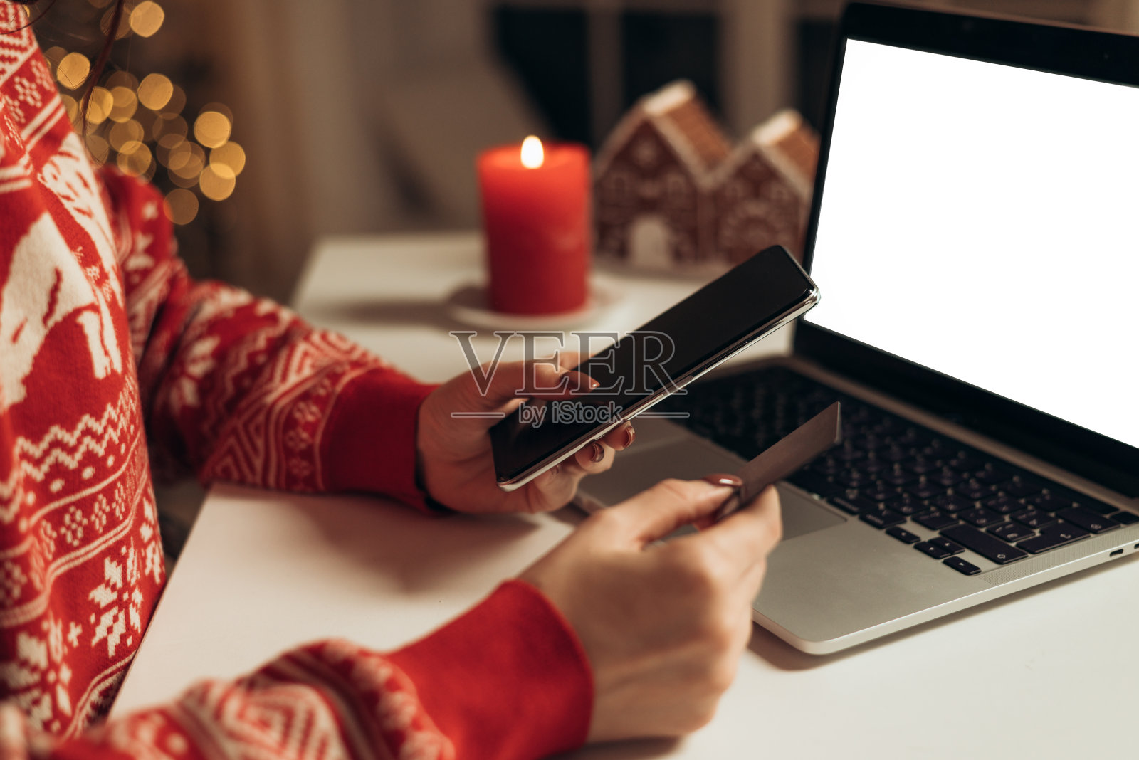 圣诞节期间，一名女子手持信用卡，在家庭办公室使用智能手机，背景是笔记本电脑照片摄影图片