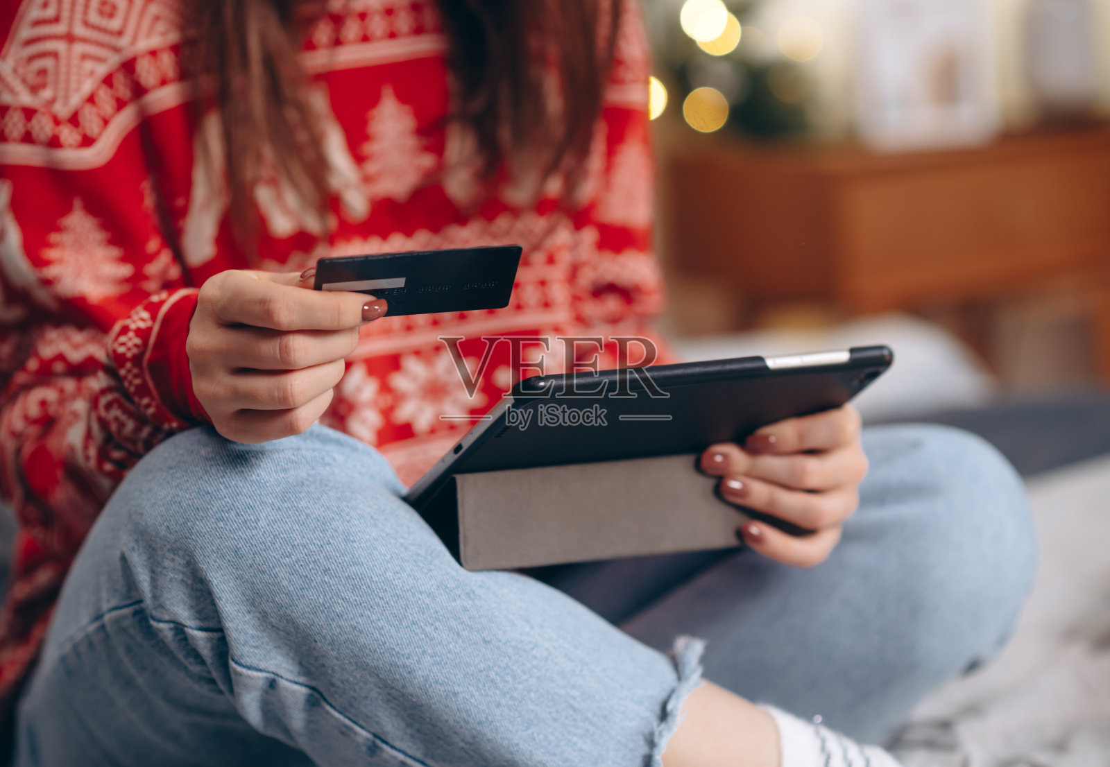圣诞节网上购物，冬季假期打折促销，在家网上购物。女性的手放在平板电脑上，带有信用卡和模糊的散景灯照片摄影图片