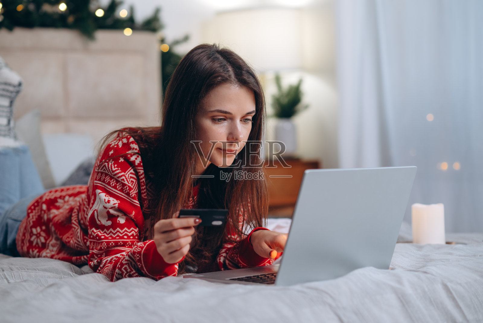 圣诞节网上购物，寒假大减价，在家网上购物。女人躺在床上，笔记本电脑上有信用卡和圣诞装饰品照片摄影图片