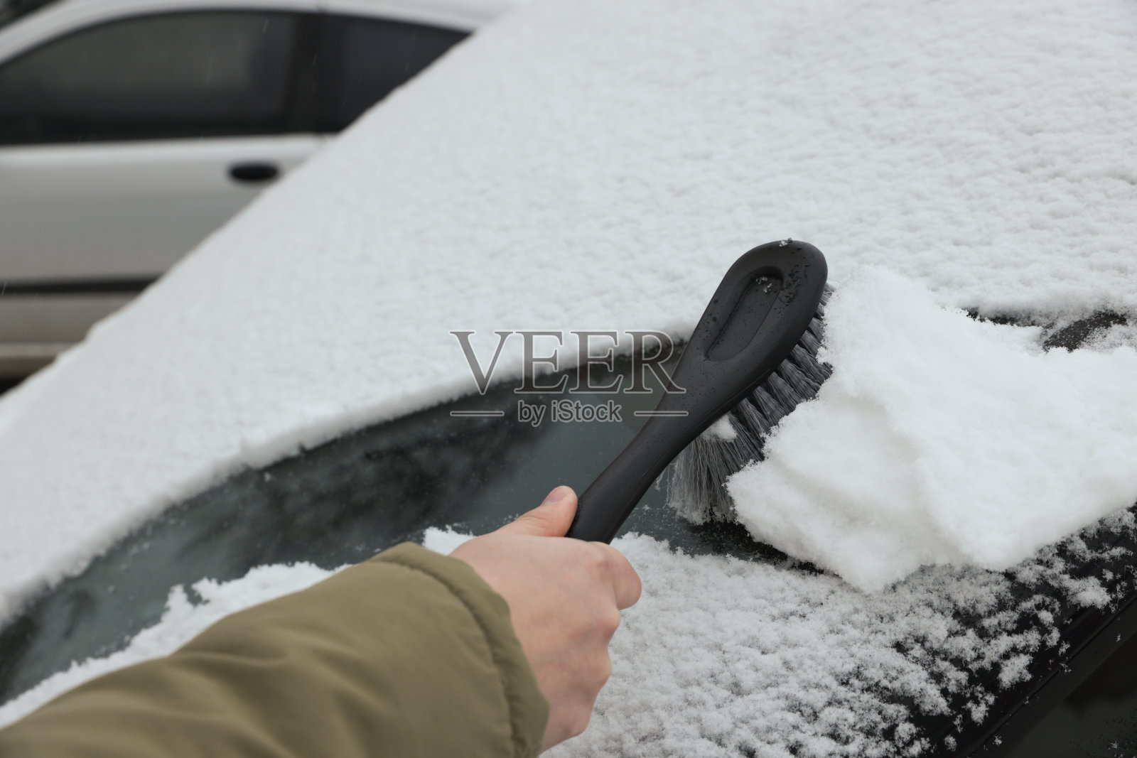 一名妇女在户外用刷子清理汽车挡风玻璃上的雪，特写照片摄影图片