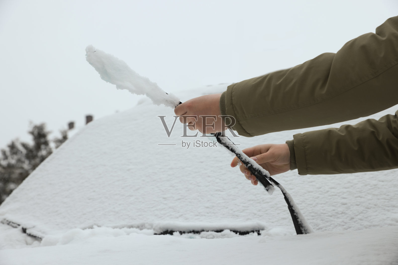 一名妇女在室外清洗被雪覆盖的汽车雨刷片，特写照片摄影图片